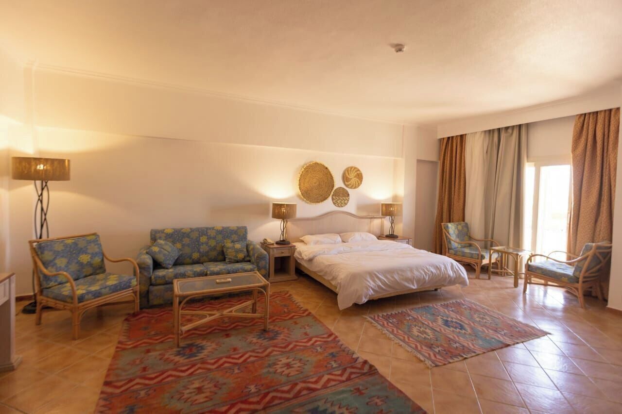 A hotel room with a bed, two armchairs, a sofa, a coffee table, and a nightstand.