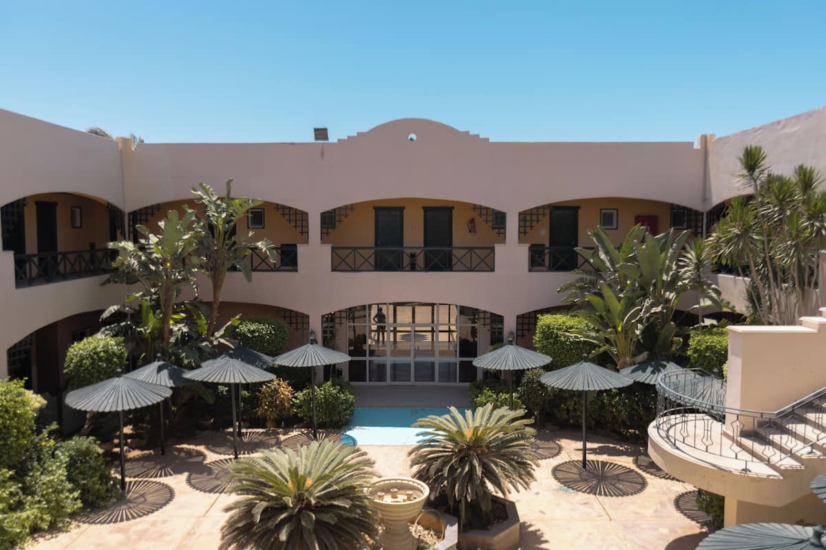 A courtyard with a pool, palm trees, and umbrellas.