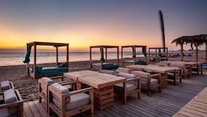 A beachside deck with wooden tables and chairs, some with cushions, and a few covered by umbrellas. - Paradise Kitesurfing Hotel (Ras Sudr)