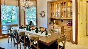 A dining area with a wooden table, chairs, a chandelier, and a view of the outdoors.