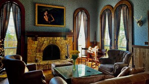 A cozy living room with a stone fireplace, leather furniture, and large windows with curtains.