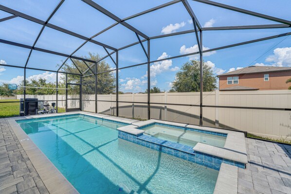 Une piscine extérieure couverte, dotée d’une structure de toit transparente, entourée d’une terrasse en briques et d’une clôture en bois.