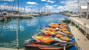 Ein Yachthafen mit mehreren vertäuten Booten und einer Reihe von Jetskis am Kai.