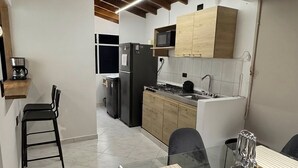 A compact kitchen with a refrigerator, stove, and wooden cabinets. There is a dining area with a glass table and chairs. - Spacious 3-bedroom apartment with AC, Laureles-Estadio, Terrace (Medellín)