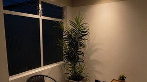 A corner room with a large window, a potted plant, a chair, and a small table. - Spacious 3-bedroom apartment with AC, Laureles-Estadio, Terrace (Medellín)
