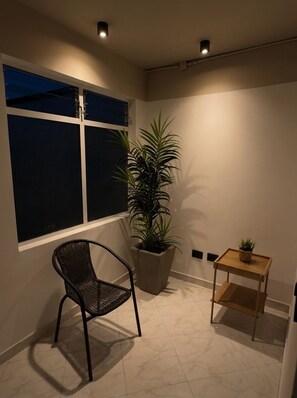 Ein Eckzimmer mit großem Fenster, einem Blumentopf, einem Stuhl und einem kleinen Tisch.
