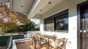 Une terrasse avec une table et des chaises en bois, une porte vitrée et une vue sur des arbres et un bâtiment.