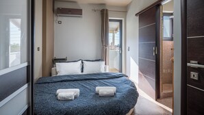 Une chambre avec un lit, deux serviettes, une fenêtre, un appareil de climatisation et une porte donnant sur un balcon.