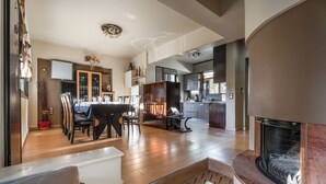 Un vaste espace de vie doté d’une cheminée, d’une table à manger avec des chaises, et d’une cuisine en arrière-plan.