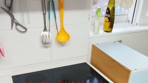 Une cuisine dotée d’une plaque de cuisson à induction noire, de meubles blancs et de divers ustensiles suspendus au-dessus.