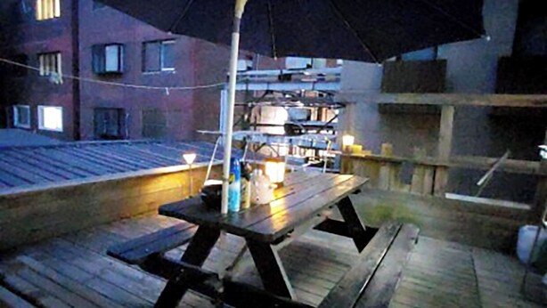 Une terrasse en bois avec une table de pique-nique et un parasol, entourée d’immeubles.
