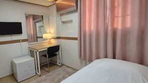 Une chambre d’hôtel avec un lit, un bureau, une chaise, une télévision et une fenêtre avec des rideaux.