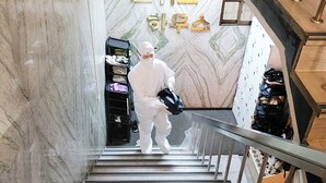 Une personne descend un escalier en marbre orné de rampes métalliques, qui mène à une pièce où sont exposées des chaussures et où est affiché un panneau dans une langue étrangère.