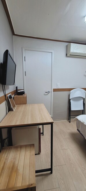 Une petite pièce avec une table en bois, un téléviseur, une porte blanche et une chaise blanche.