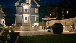 Casa de dos pisos con un patio que incluye mobiliario exterior y una parrilla.