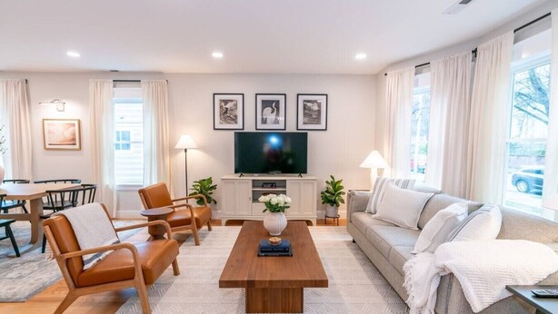 Una sala de estar moderna con una mesa de centro de madera, sillones de cuero, un sofá gris y un televisor de pantalla plana montado en la pared.
