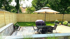 Un patio trasero con una parrilla, mesa y sillas de exterior, y un cerco de madera.