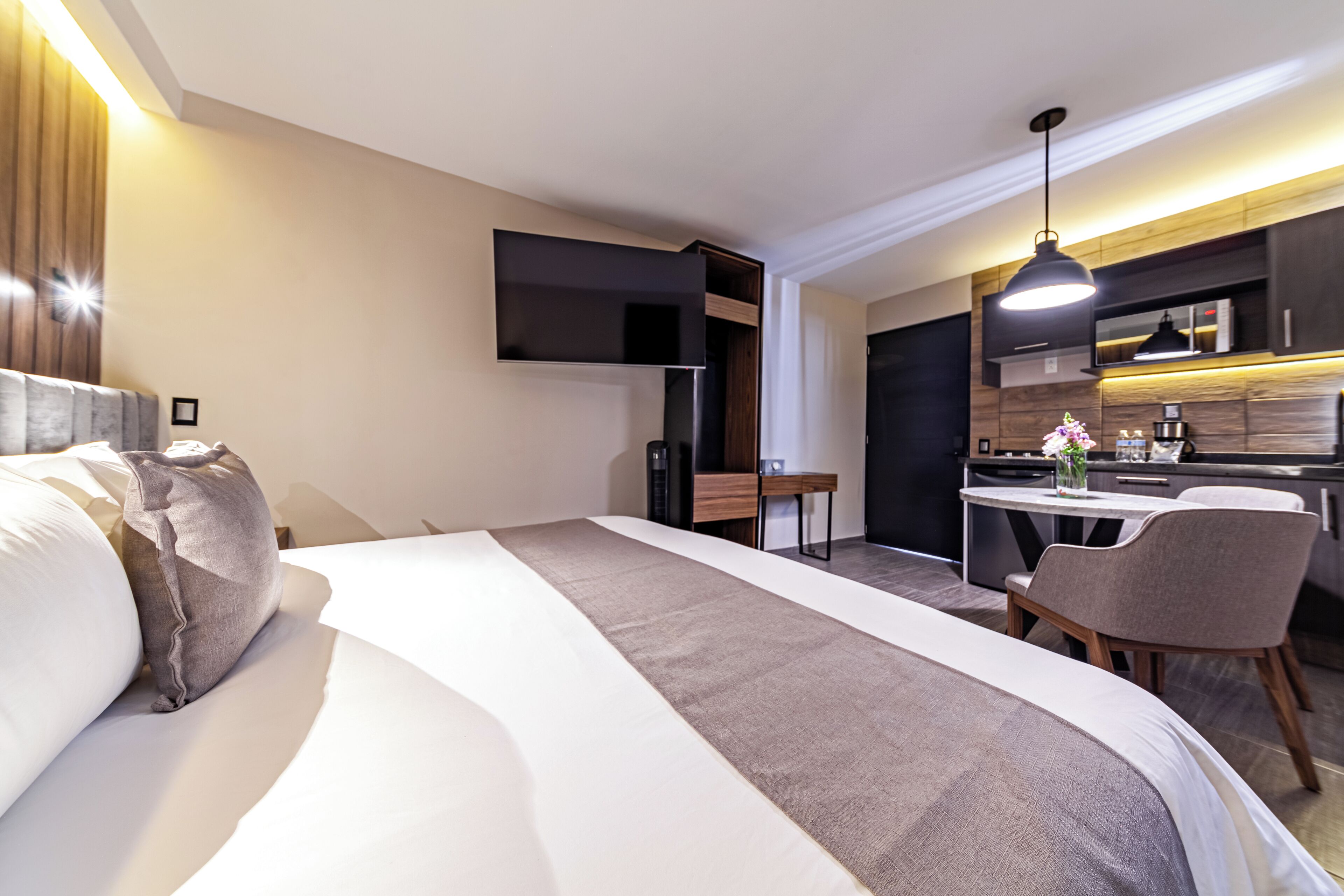 A modern hotel room with a large bed, a desk, and a kitchenette.