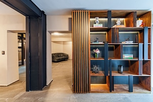Un interior moderno con una estantería de madera, un sofá negro y un pasillo que conduce a otra habitación.