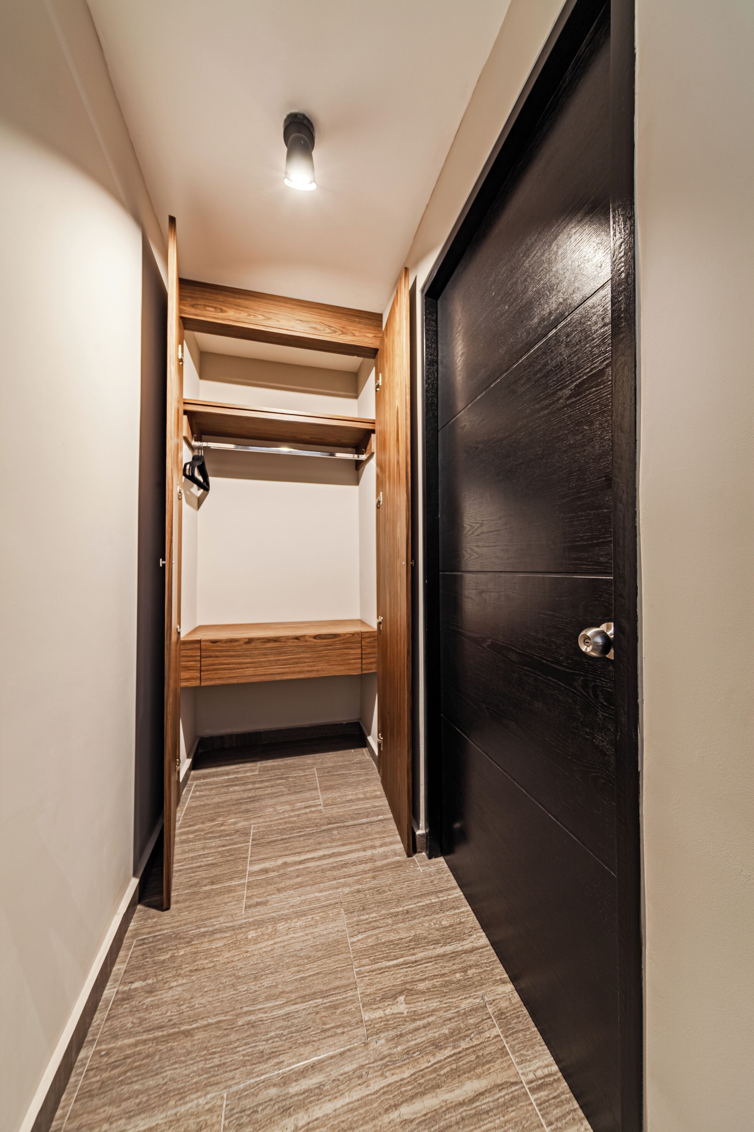 Un pasillo con un banco de madera, una puerta negra y una lámpara en el techo.
