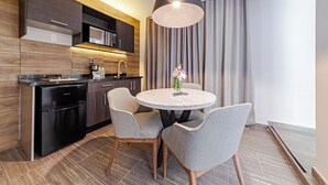 A modern kitchen with dark wood cabinetry, a black dishwasher, and a round dining table with two grey chairs. - CASA NOU (Mexico City)