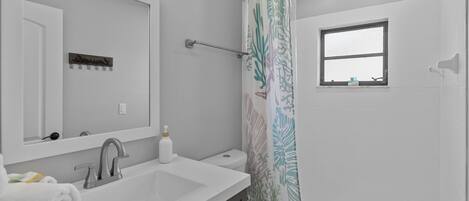 Un baño con un lavamanos blanco, un espejo, un inodoro y una cortina de ducha con diseño de hojas.