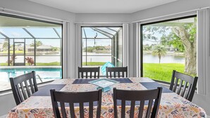 Comedor con mesa y sillas, ventanas amplias con vista a una piscina y follaje.