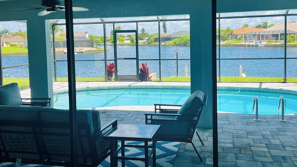 Zona de piscina con vistas a un lago, mobiliario exterior y un porche cubierto.