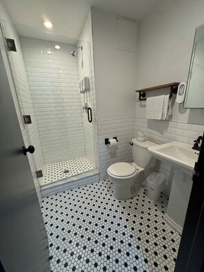 Une salle de bain avec douche, toilettes, lavabo et carrelage au sol.