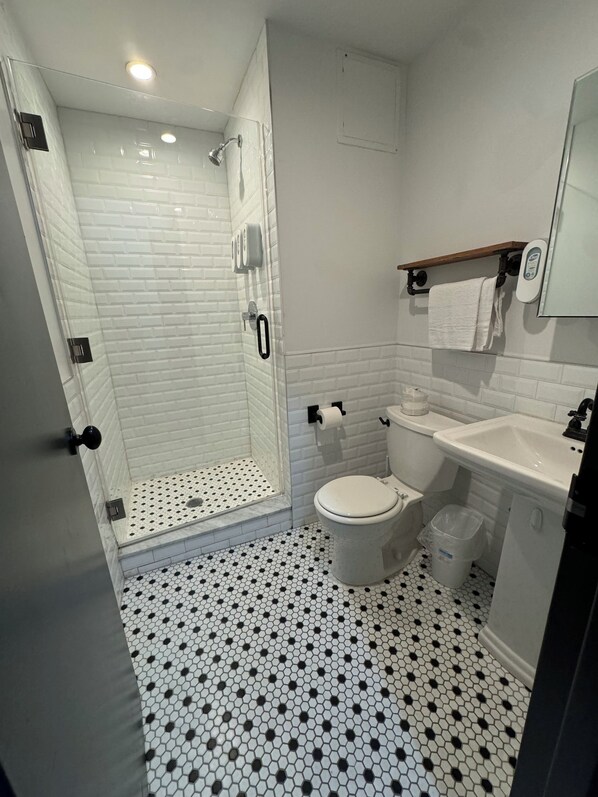 A bathroom with a shower, toilet, sink, and tiled floor. - Tribeca Hotel FiDi (New York)