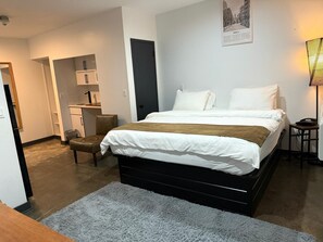 Une chambre à coucher avec un lit, un bureau, une chaise, une porte et une lampe.