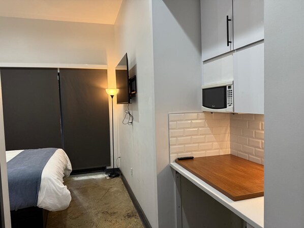 Une chambre d’hôtel compacte comprenant un lit, une lampe de chevet, un four à micro-ondes et un petit coin cuisine.