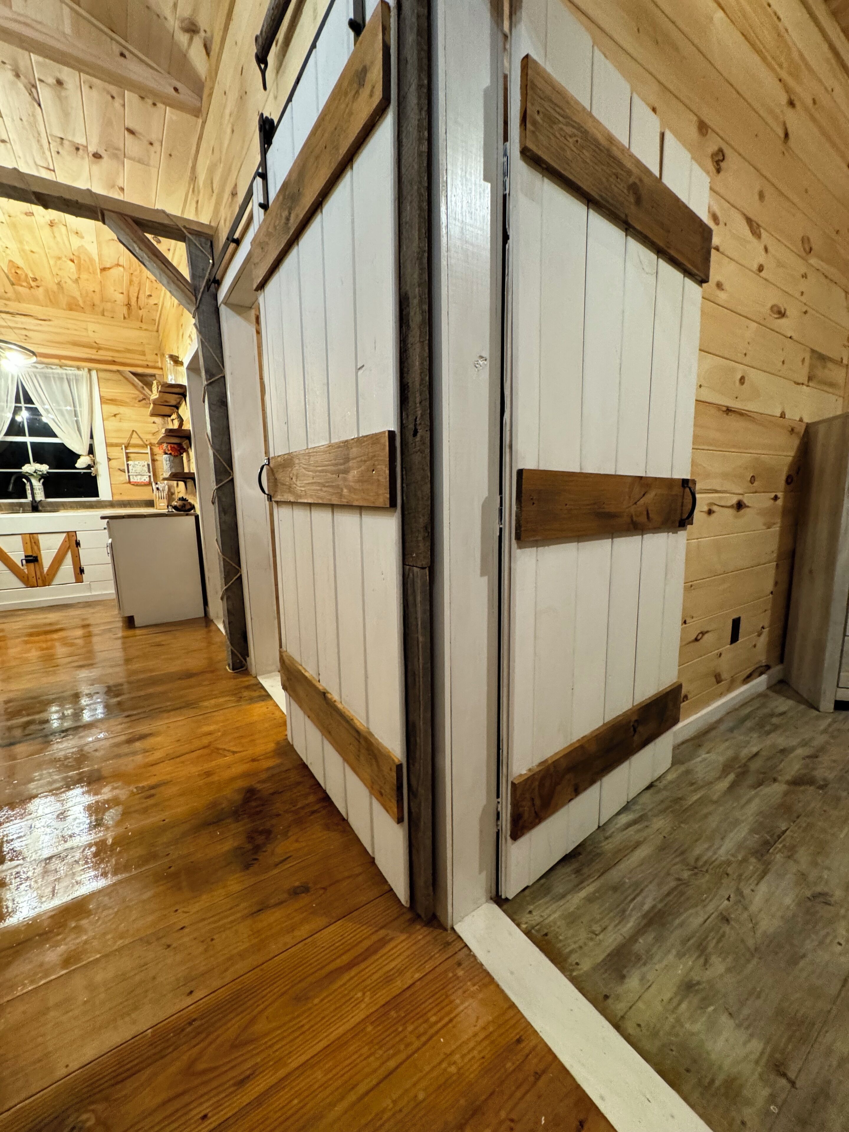 A wooden interior with a sliding door, wooden flooring, and a window with curtains.