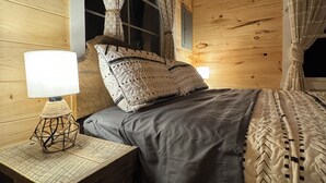 Une chambre dans une cabane en bois, avec un lit, une table de chevet, une lampe et des rideaux.