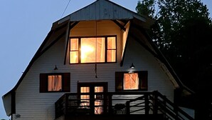 Une grande grange à deux étages, dotée d  ’une entrée avant abritée et d’un escalier en bois menant à un balcon.