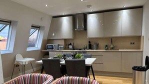 Een moderne keuken met roestvrijstalen kastjes, een eethoek met gestreepte stoelen, en een kleine witte stoel.