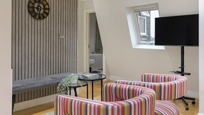 Een moderne woonkamer met een gestreept bankstel, een ronde wandklok en een flatscreen televisie.