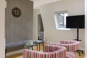 A modern living room with a striped sofa set, a round wall clock, and a flat-screen TV. - City flat near Brick Lane w/ kitchen & dining (Greater London)