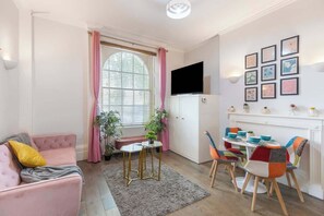 A cozy living room with a pink sofa, a small round table, and colorful chairs. - Pet-Friendly Flat near King's Cross (London)