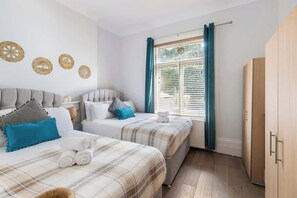 A bedroom with two beds, a wardrobe, and a window with curtains.