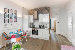 A modern kitchen with white cabinets, a microwave, and a stove. There is a dining area with colorful chairs and a table.