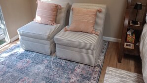 Une pièce avec deux fauteuils à rayures, un tapis à motifs, un plancher en bois et une fenêtre laissant entrer la lumière naturelle.