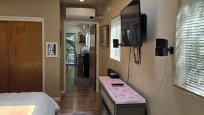Une chambre avec un grand lit, un bureau avec un ordinateur, un téléviseur fixé au mur et une fenêtre avec des stores.