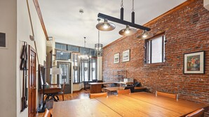 A dining area with a large wooden table, brick walls, and hanging pendant lights.