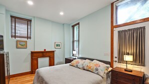 A bedroom with a bed, wooden dresser, nightstand, and a desk with a lamp.