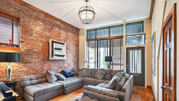A spacious living room with a large sectional sofa, a brick wall, and large windows.