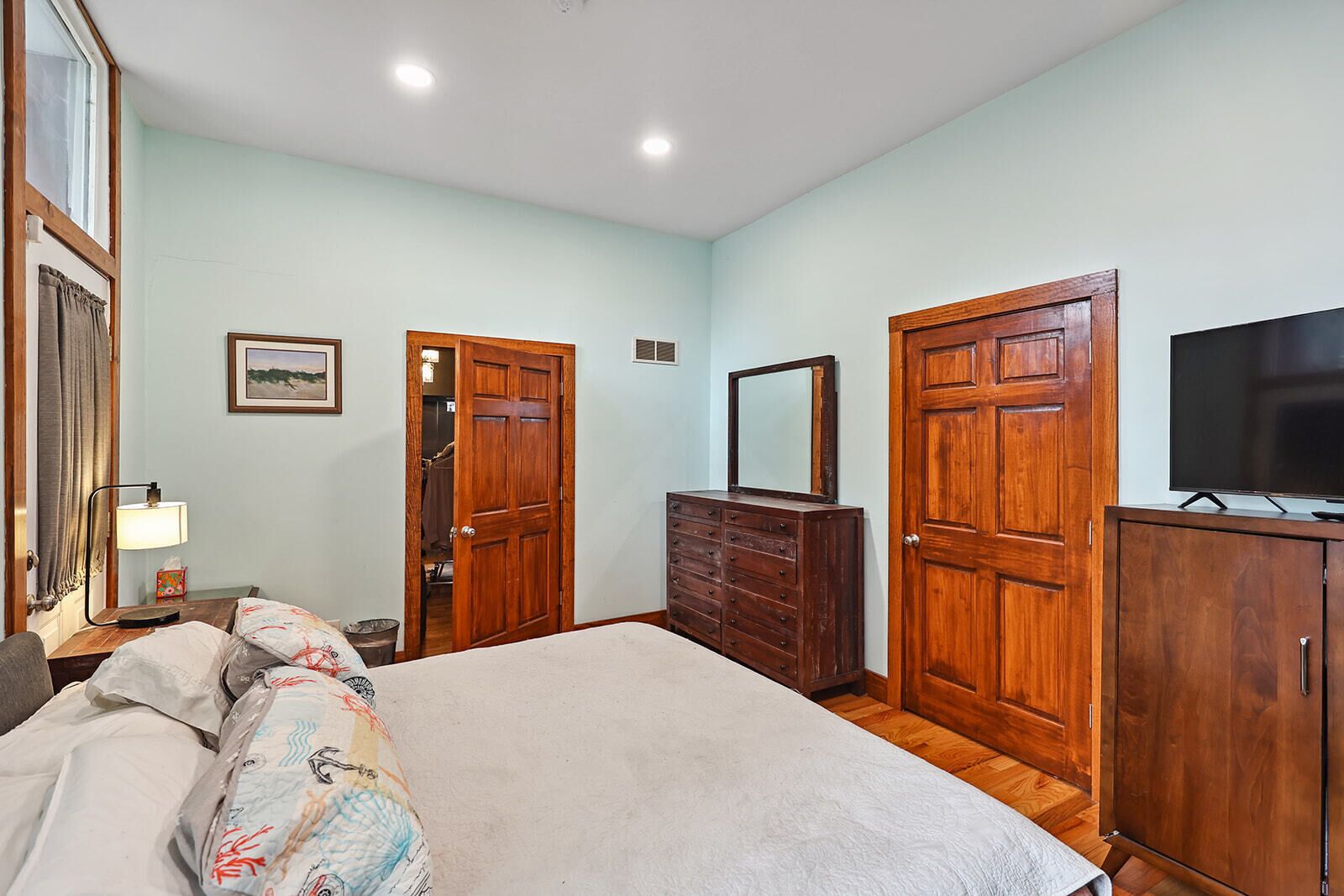 A bedroom with a bed, dresser, TV, and wooden doors.