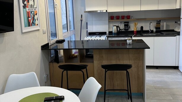 Een moderne keuken met houten kastjes, een centraal eiland en een eethoek met witte stoelen en een tafel.