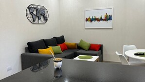 Een moderne woonkamer met een zwart aanrecht, een grijze bank met kleurrijke kussens, een witte stoel en een kunstwerk aan de muur.