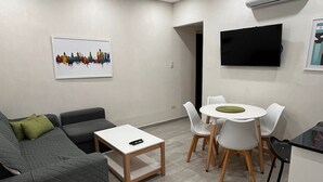 Een moderne woonkamer met een grijze bank, een klein wit tafeltje en een eetgedeelte met witte stoelen en een ronde tafel.
